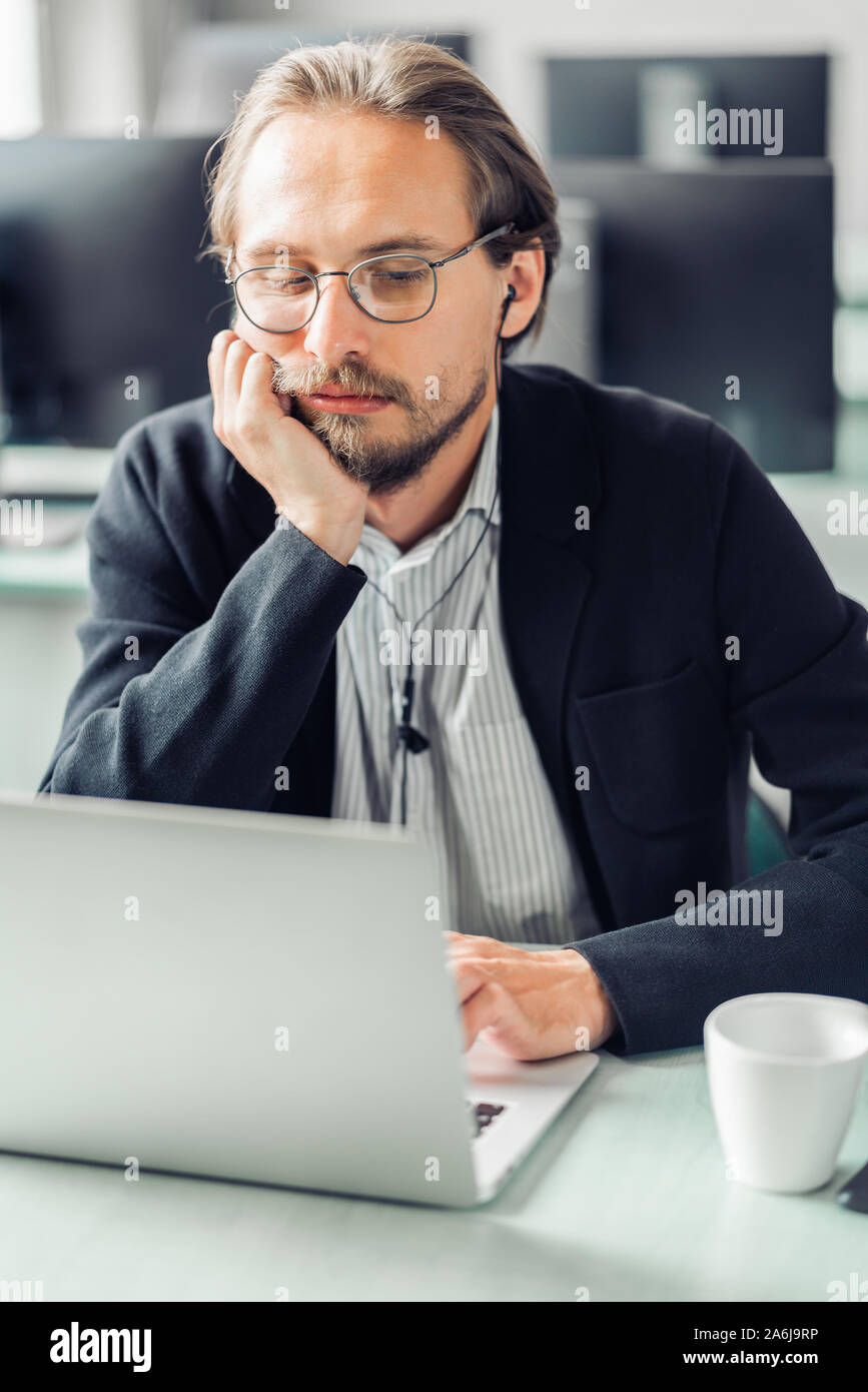 Jungen gutaussehenden Mann bei der Arbeit langweilen. Computer und eine Kaffeetasse im Vordergrund sichtbar. Stockfoto