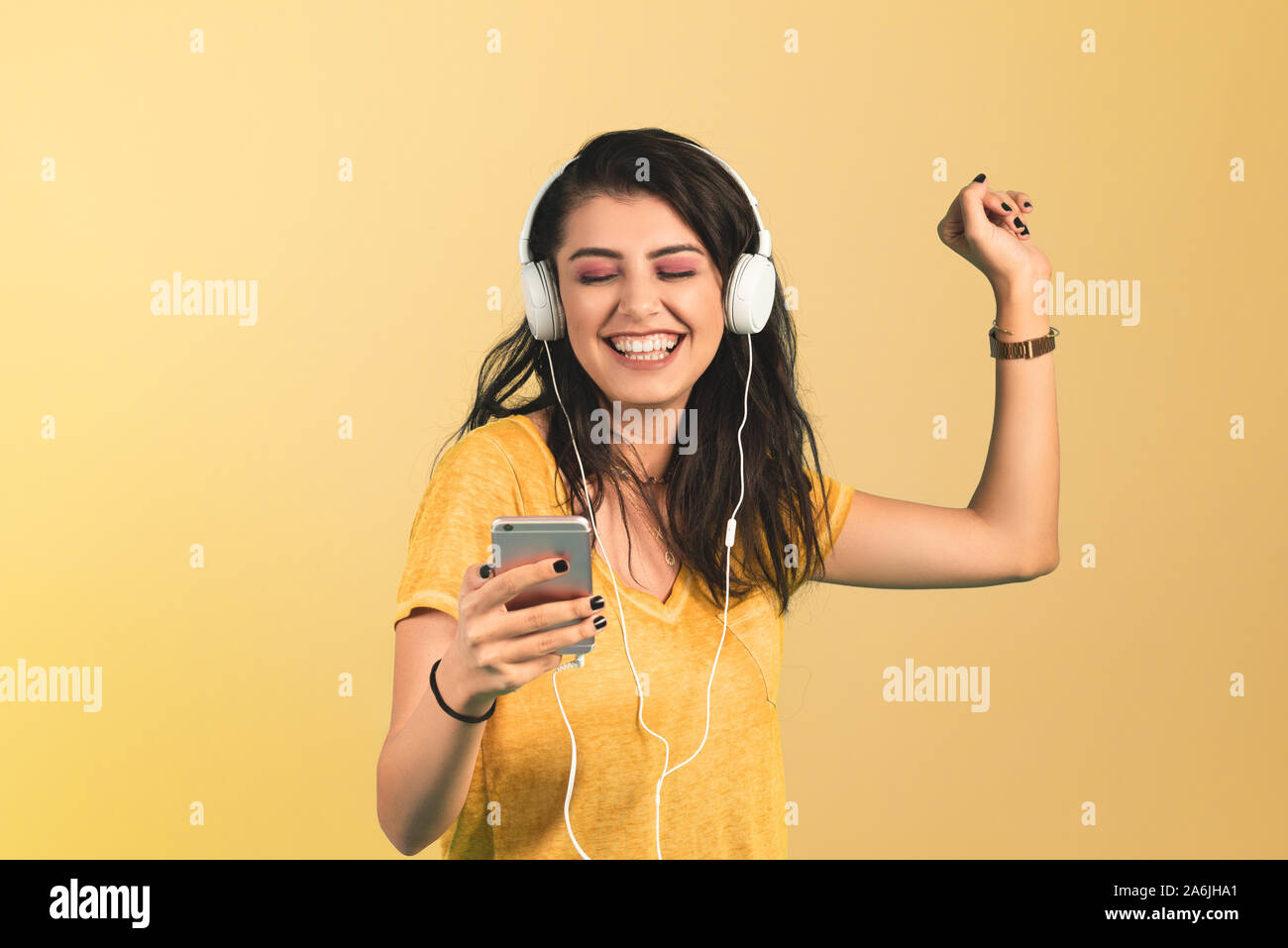 Junge Frau hört Musik mit Smartphone auf gelben Hintergrund. Stockfoto