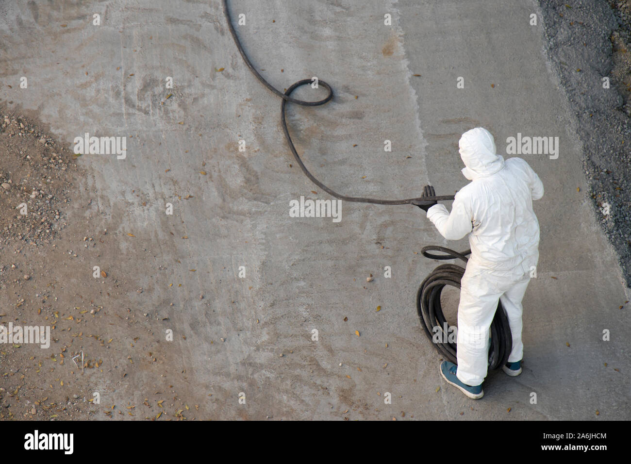 Bauarbeiter in weißer Schutzkleidung jumpsuit wickeln einen langen Schlauch, von oben Stockfoto