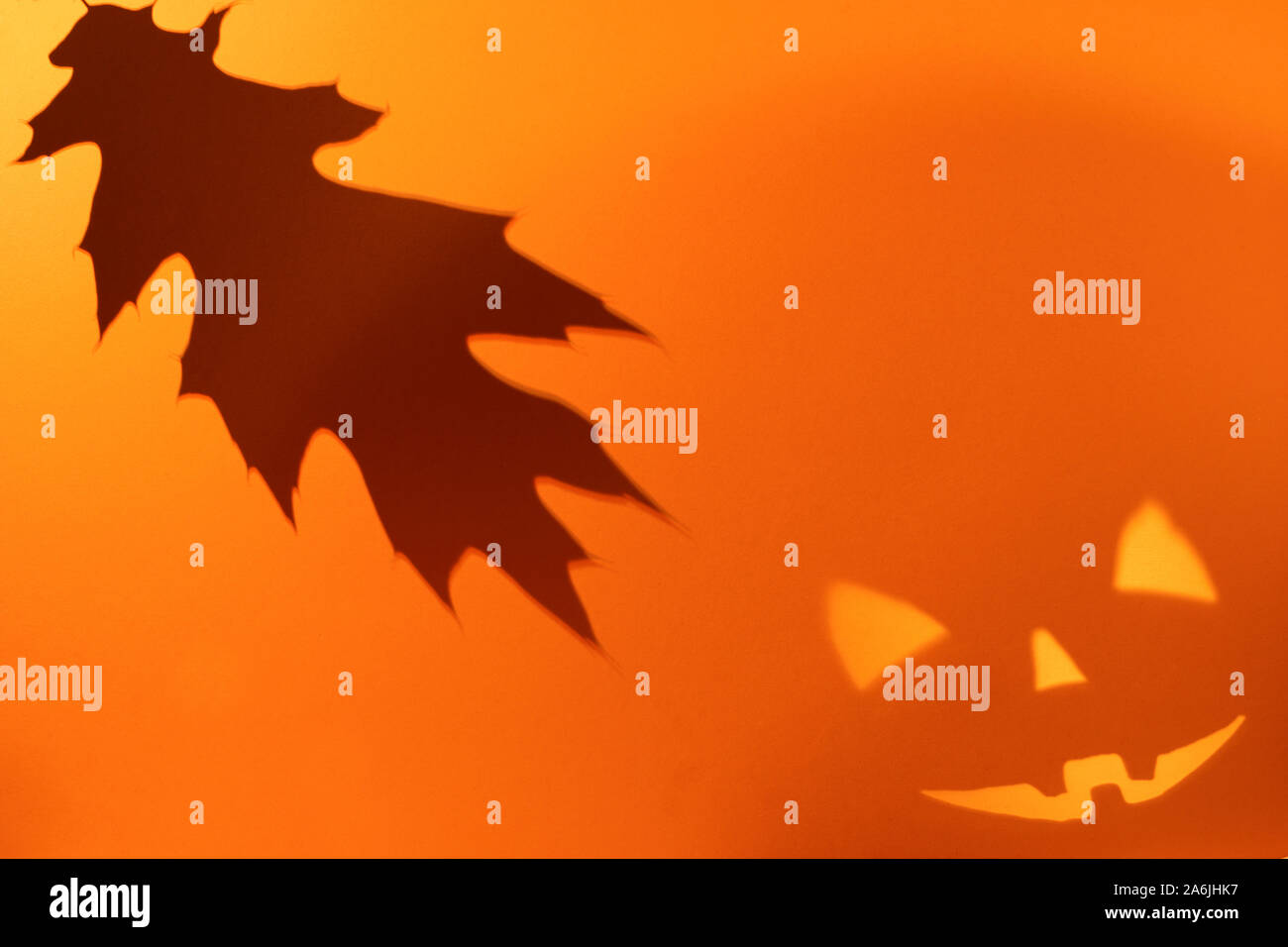 Halloween scary pumpkin Gesicht und Eichenlaub auf orangefarbenen Papier Hintergrund. Schatten aus dem Feuer. Beängstigend, Lächeln, Gesicht. Halloween Konzept. Platz kopieren Stockfoto
