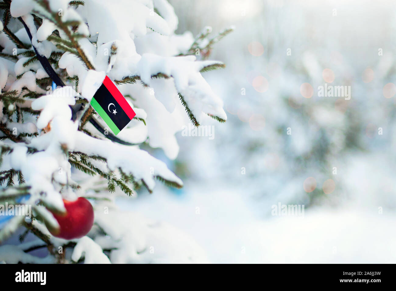 Weihnachten Libyen. Xmas Tree mit Schnee, Dekorationen und eine Flagge bedeckt. Verschneite Wald Hintergrund im Winter. Weihnachten Grußkarte. Stockfoto