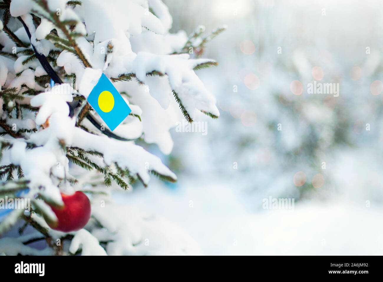 Weihnachten in Palau. Xmas Tree mit Schnee, Dekorationen und eine Flagge bedeckt. Verschneite Wald Hintergrund im Winter. Weihnachten Grußkarte. Stockfoto