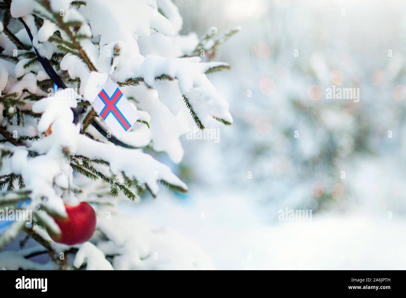 Weihnachten Färöer Inseln. Xmas Tree mit Schnee, Dekorationen und eine Flagge bedeckt. Verschneite Wald Hintergrund im Winter. Weihnachten Grußkarte. Stockfoto