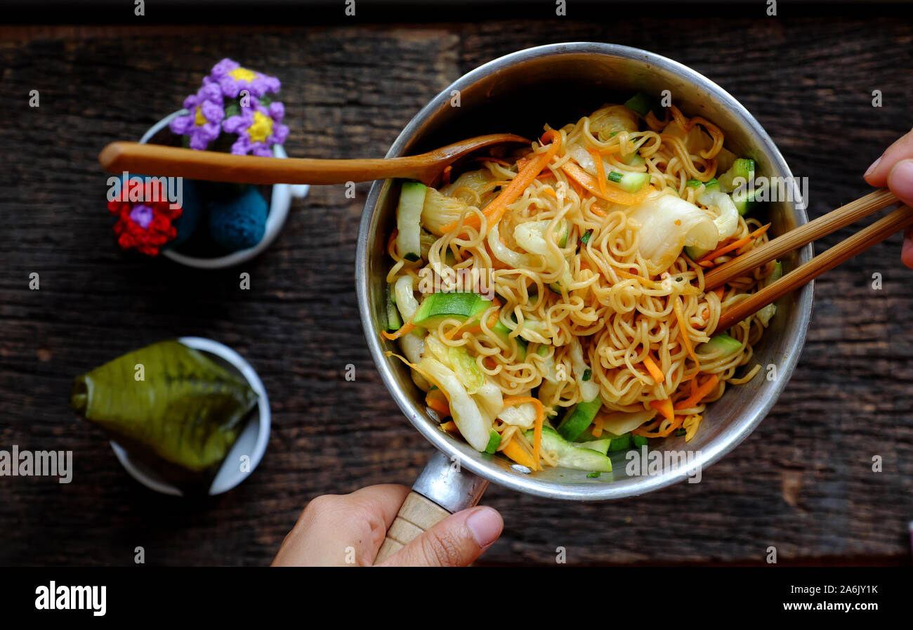 Ansicht von oben in der Nähe der menschlichen Hand mix Gelb trocken instant Nudeln mit Gemüse für schnelle Veganes Frühstück auf dunklem Hintergrund Stockfoto