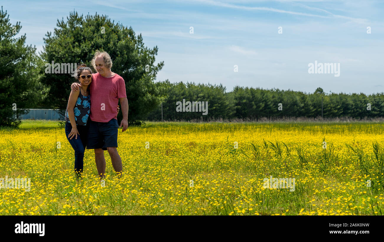 Paar stehend in das große Feld mit gelben Blumen und Bäume im Hintergrund auf der Suche nach Fotograf Stockfoto