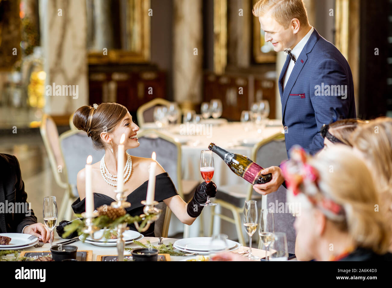 Elegant gekleidete Menschen mit einem festlichen Abendessen während einer Silvester im luxuriösen Restaurant, Kellner serviert Gerichte und Abfüllung Weingläser Stockfoto