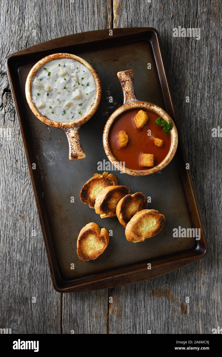 Zwei frische, hausgemachte Schalen von Clam Chowder und Tomatensuppe mit Knoblauch Toast auf einem Backblech. Stockfoto