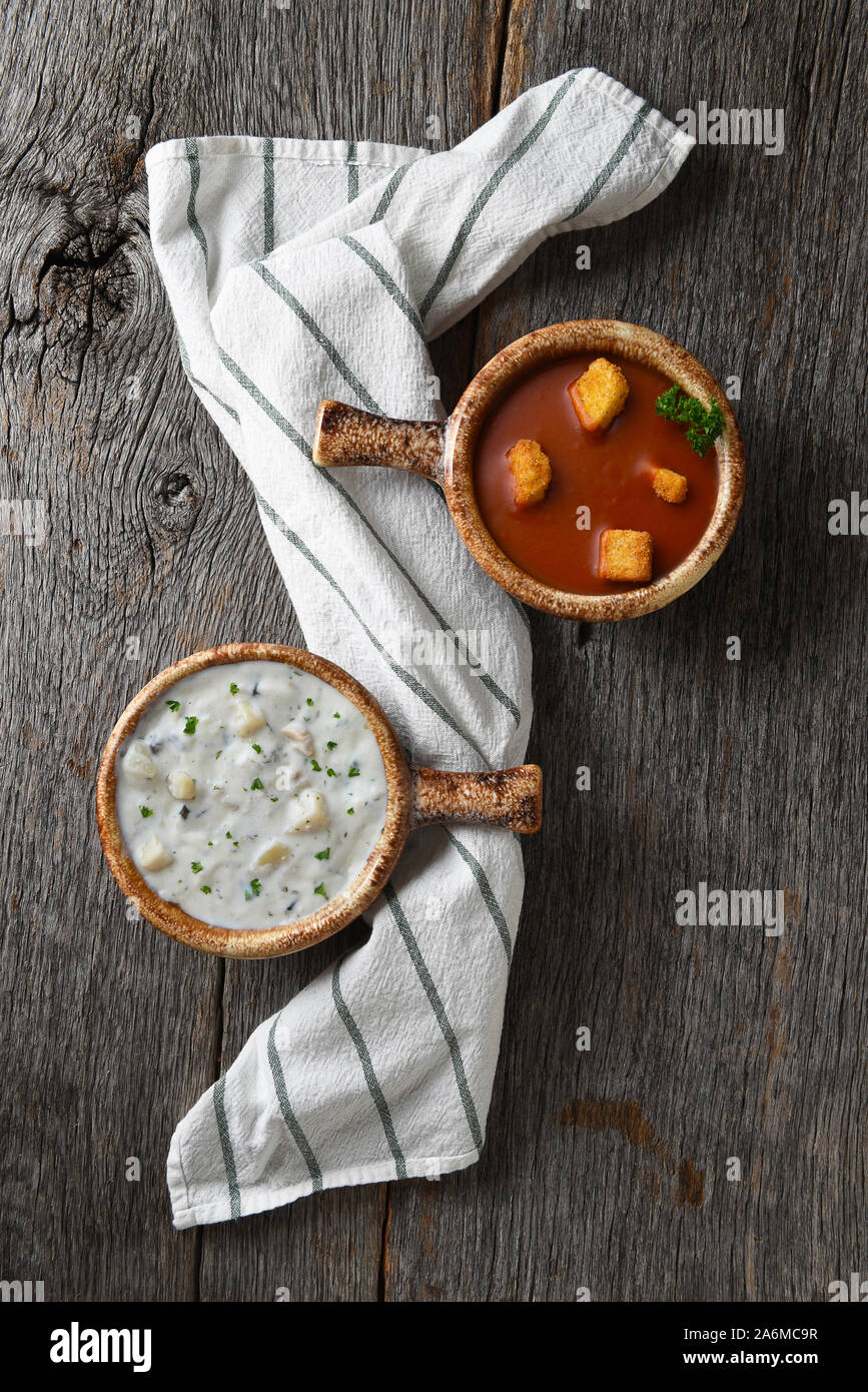 Flach mit zwei Schalen mit hausgemachten Clam Chowder und Tomaten Suppe auf einem rustikalen Holztisch mit einem Küchentuch. Stockfoto