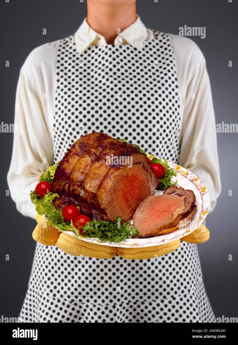 Nahaufnahme einer Hausfrau in einer Schürze und ofenhandschuhe Holding eine Platte mit Roastbeef, mit garnieren, in Scheiben geschnitten. Stockfoto