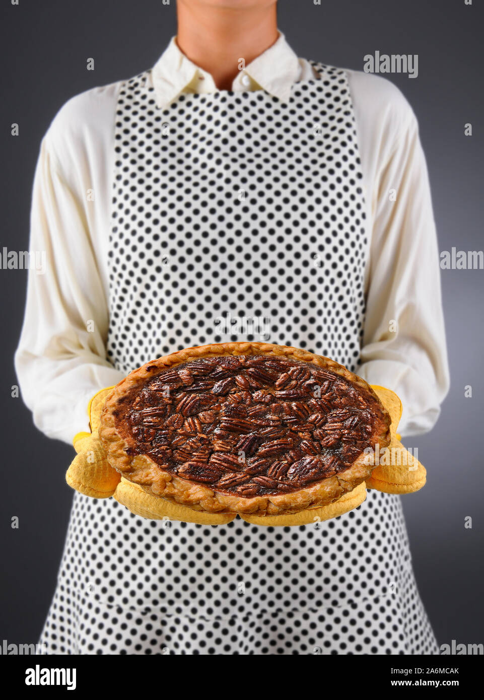 Nahaufnahme einer Hausfrau in einer Schürze und ofenhandschuhe Holding einen frisch gebackenen Urlaub Pecan Pie. Stockfoto