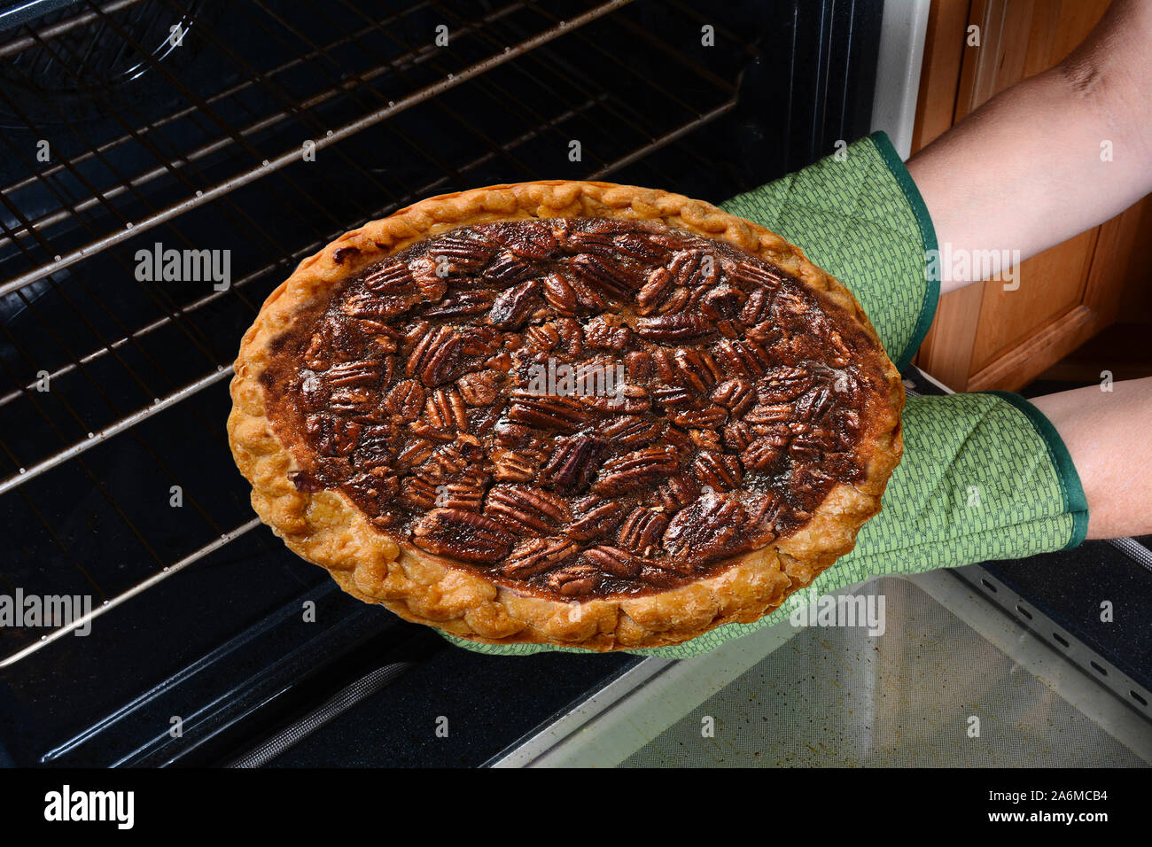 Nahaufnahme einer Frau einen frisch gebackenen Pecan Pie aus dem Ofen. Horizontale zeigt nur die womans Hände in Ofenhandschuhe. Stockfoto