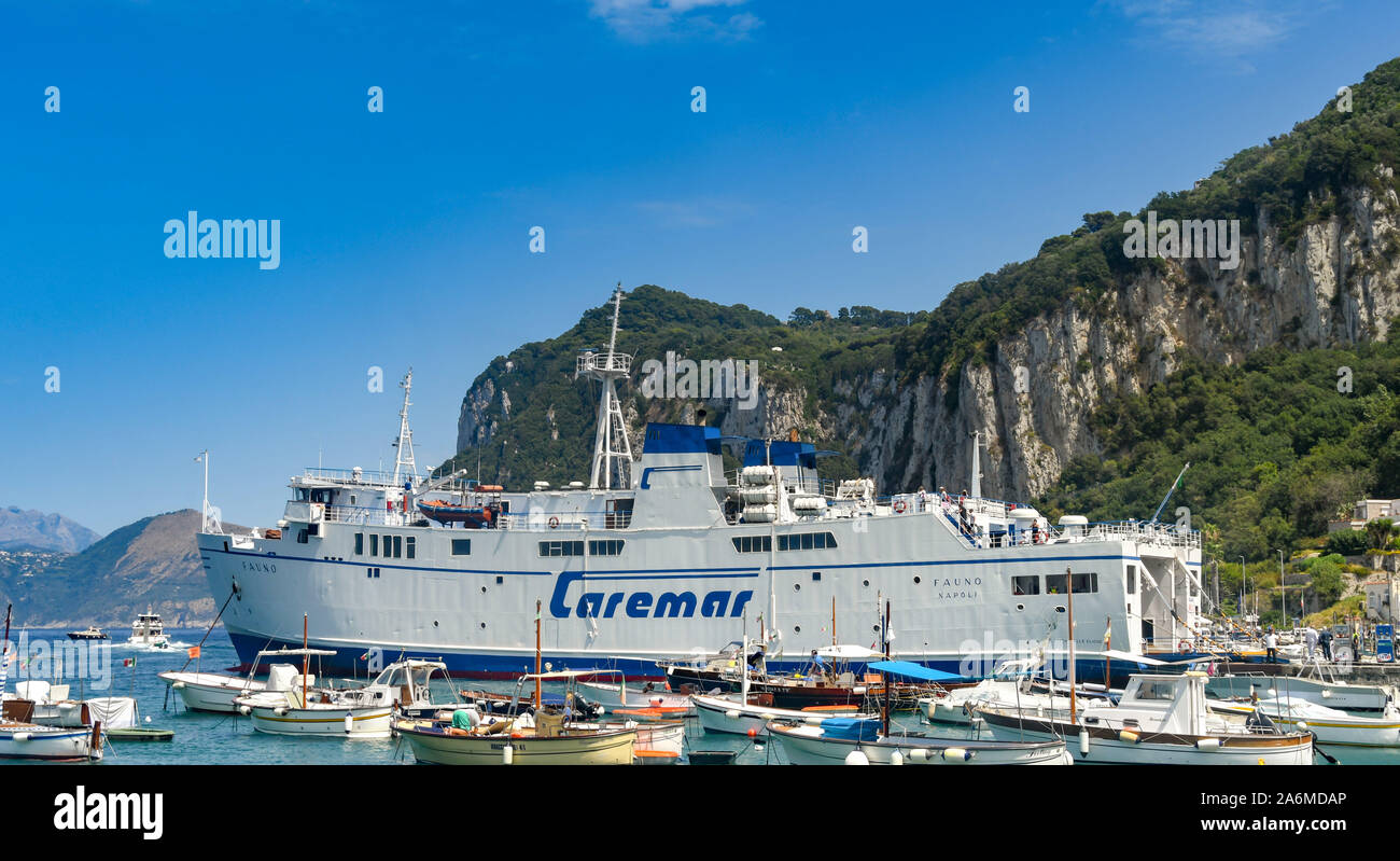 Insel Capri, Italien - AUGUST 2019: Große Autofähre betrieben von caremar unter kleinen Fischerboote im Hafen auf der Insel Capri angedockt. Stockfoto