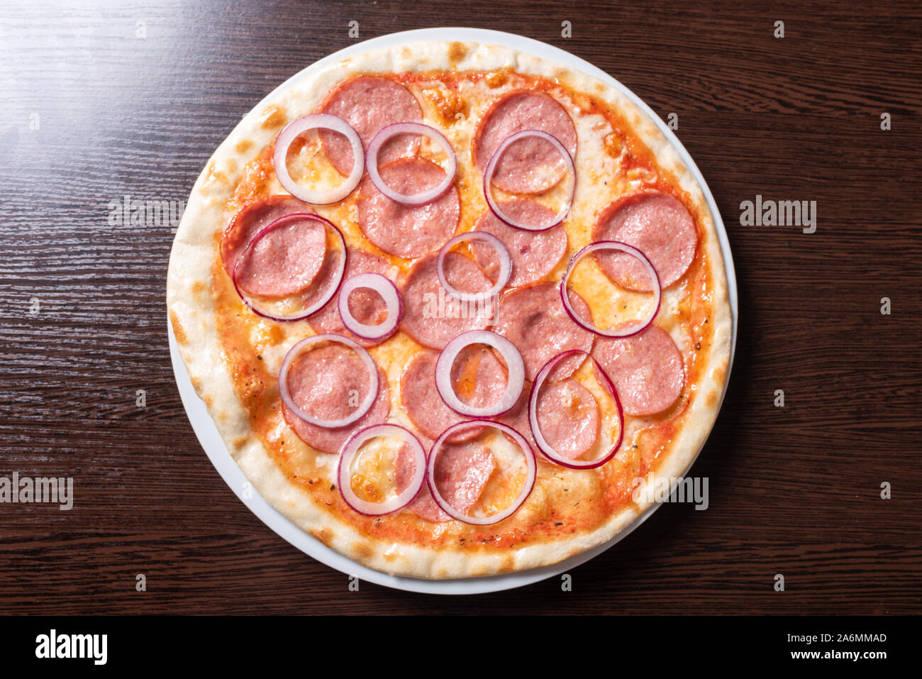 Billige Pizza mit Salami, Zwiebeln, in Tomatensauce. Stockfoto