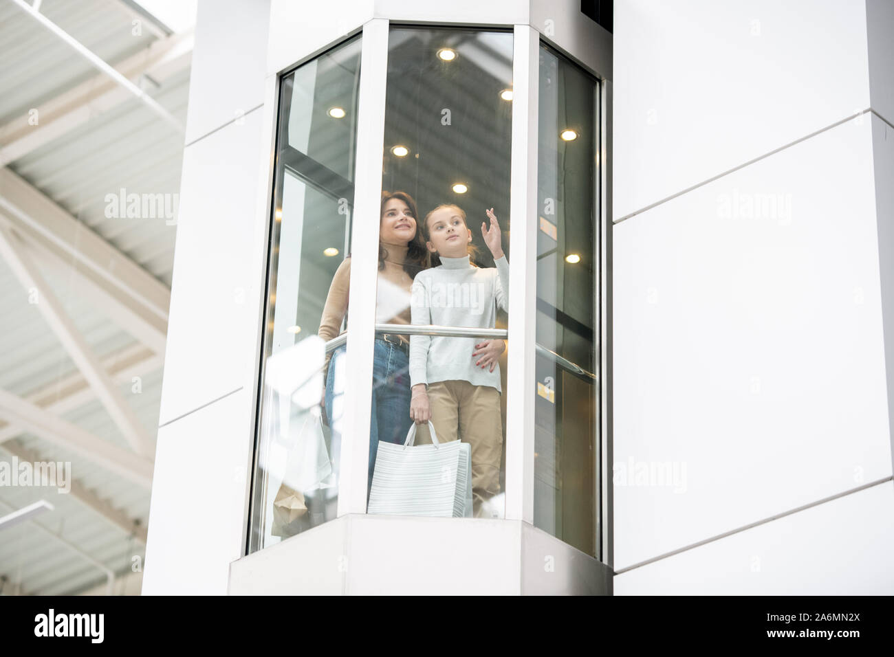 Junge Mutter und Tochter etwas diskutieren während der Bewegung nach oben im Elevator Stockfoto