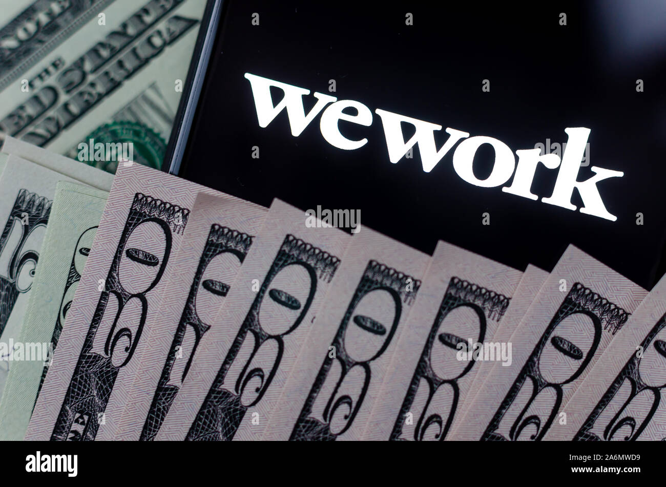 WeWork Firmenlogo auf den Bildschirm des Smartphones und Dollarscheine um ihn herum. WeWork bietet Büro- und Arbeitsbereich Lösungen. Konzept Foto. Stockfoto