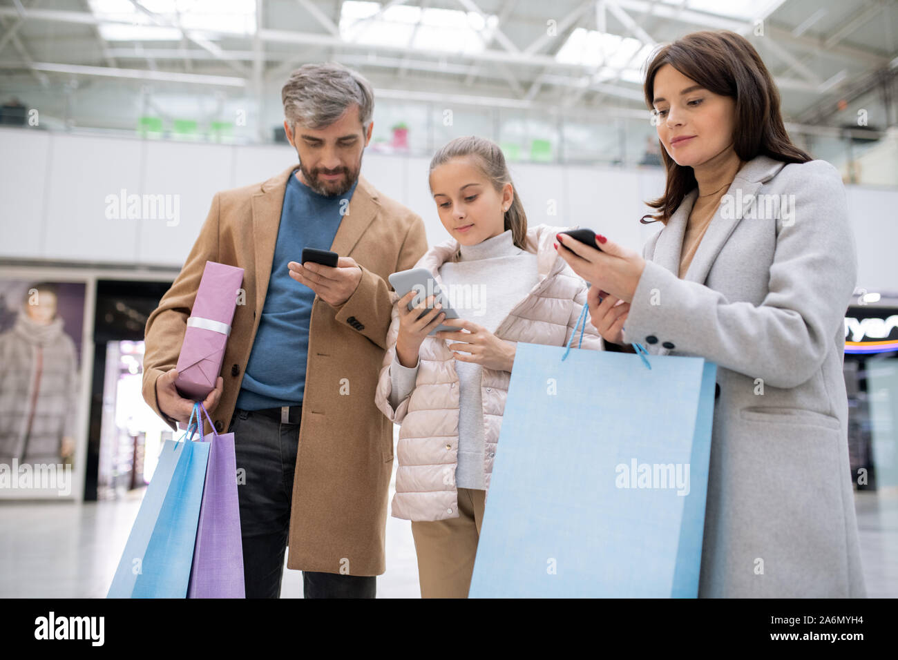 Drei zeitgenössische Shopaholics mit Smartphones Scrollen durch Online Shops Stockfoto