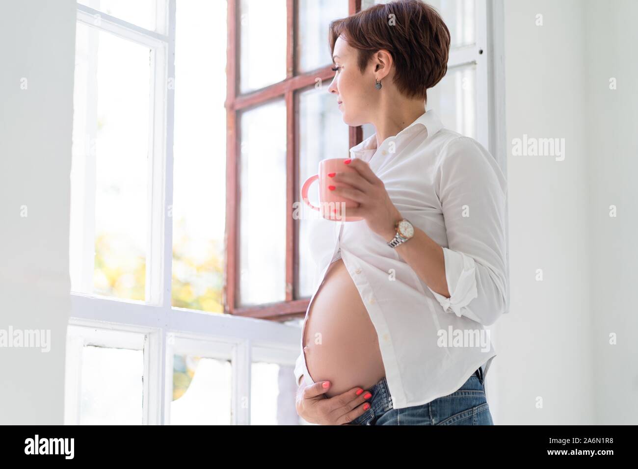 Schwangerschaft Konzept. Stilvolle Middle-Aged Frau steht mit einem rosa Schale Stockfoto