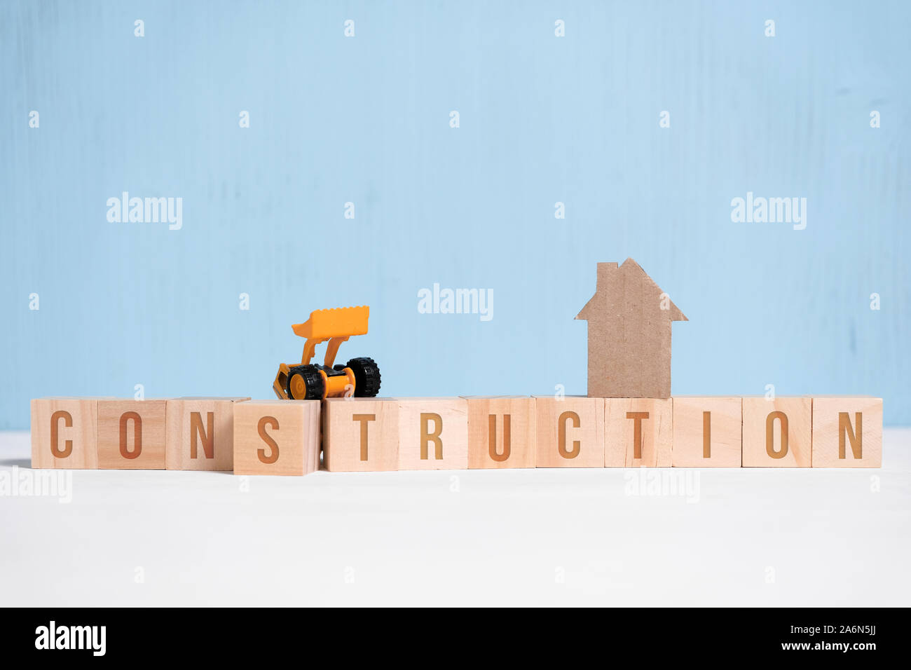 Abstrakte Pappe Haus neben Holzwürfel mit Inschriften und Baumaschinen. Bau Konzept. Close Up. Stockfoto