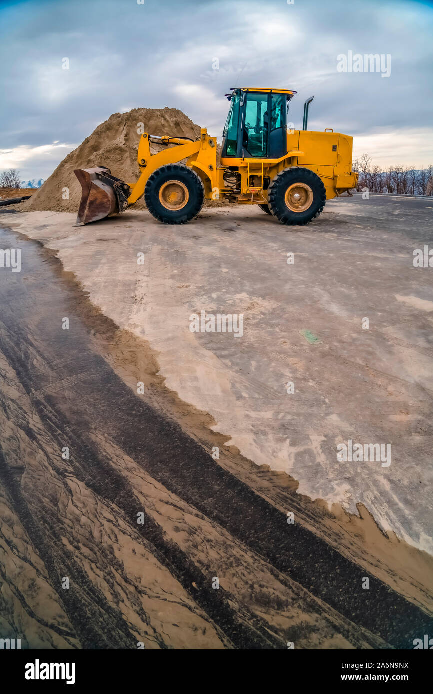 Gelben Bulldozer auf einer Straße mit Damm von Boden und bewölkter Himmel Hintergrund Stockfoto