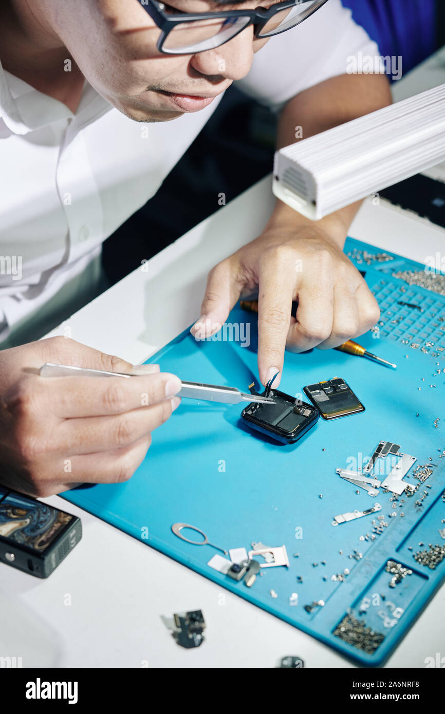 Handwerker in Gläsern mit einer Pinzette bei der Festsetzung der Schnüre in gebrochenen Smartwatch Stockfoto