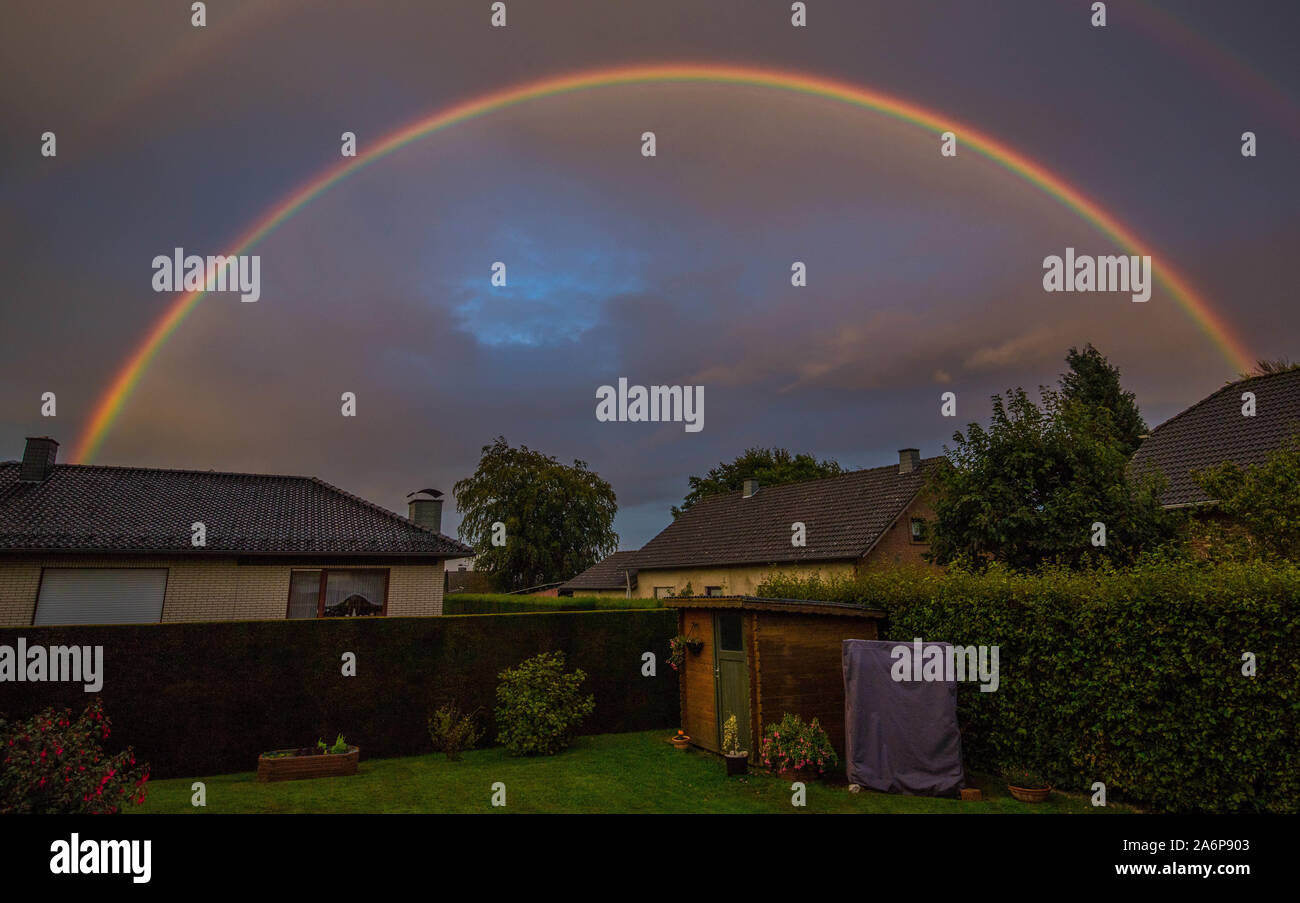 Regenbogen über Häuser in einem Dorf in der Eifel. Helle Farben vor einem dunklen Himmel. Stockfoto