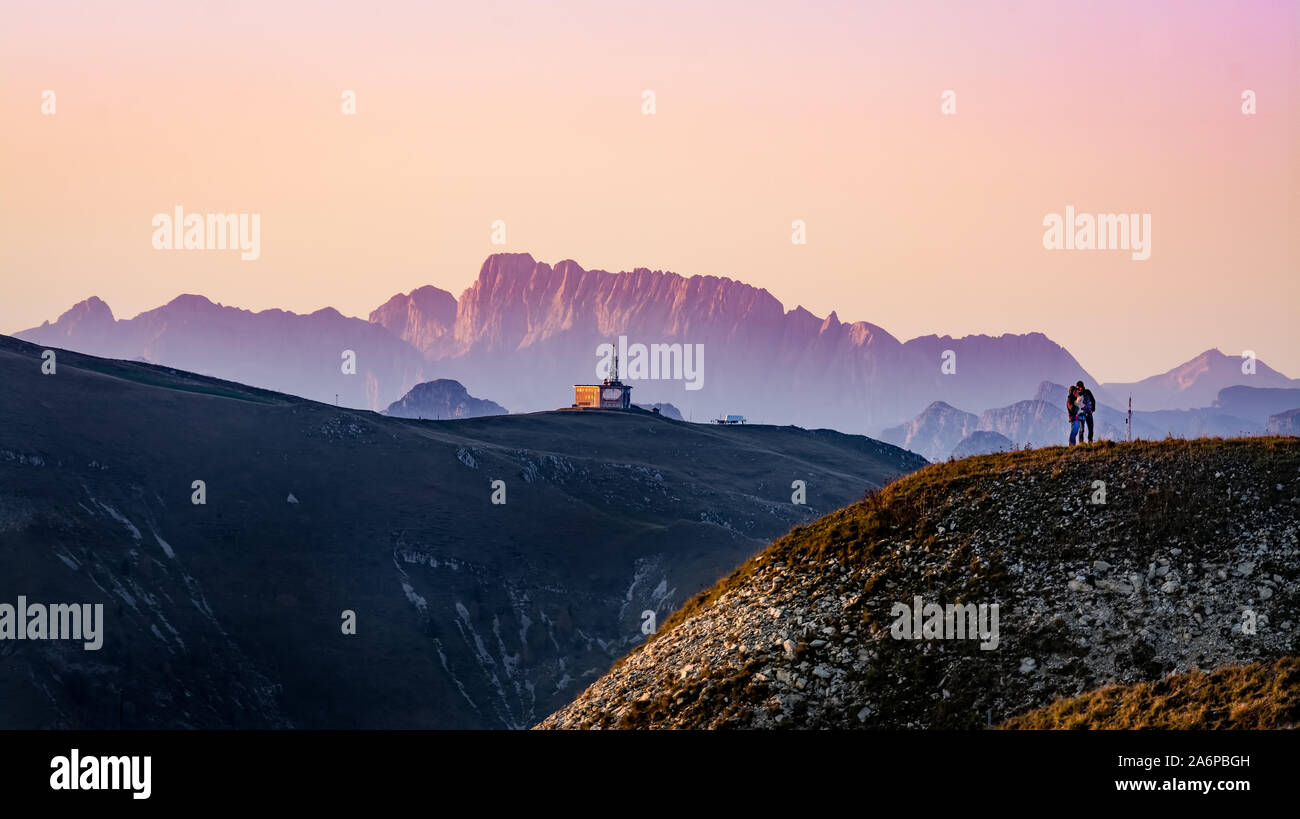 Ein paar Leute stehen auf dem Gipfel des Mount Pizzoc (Venetien, Italien) bei Sonnenuntergang im Herbst. Alpen und Dolomiten im Hintergrund Stockfoto