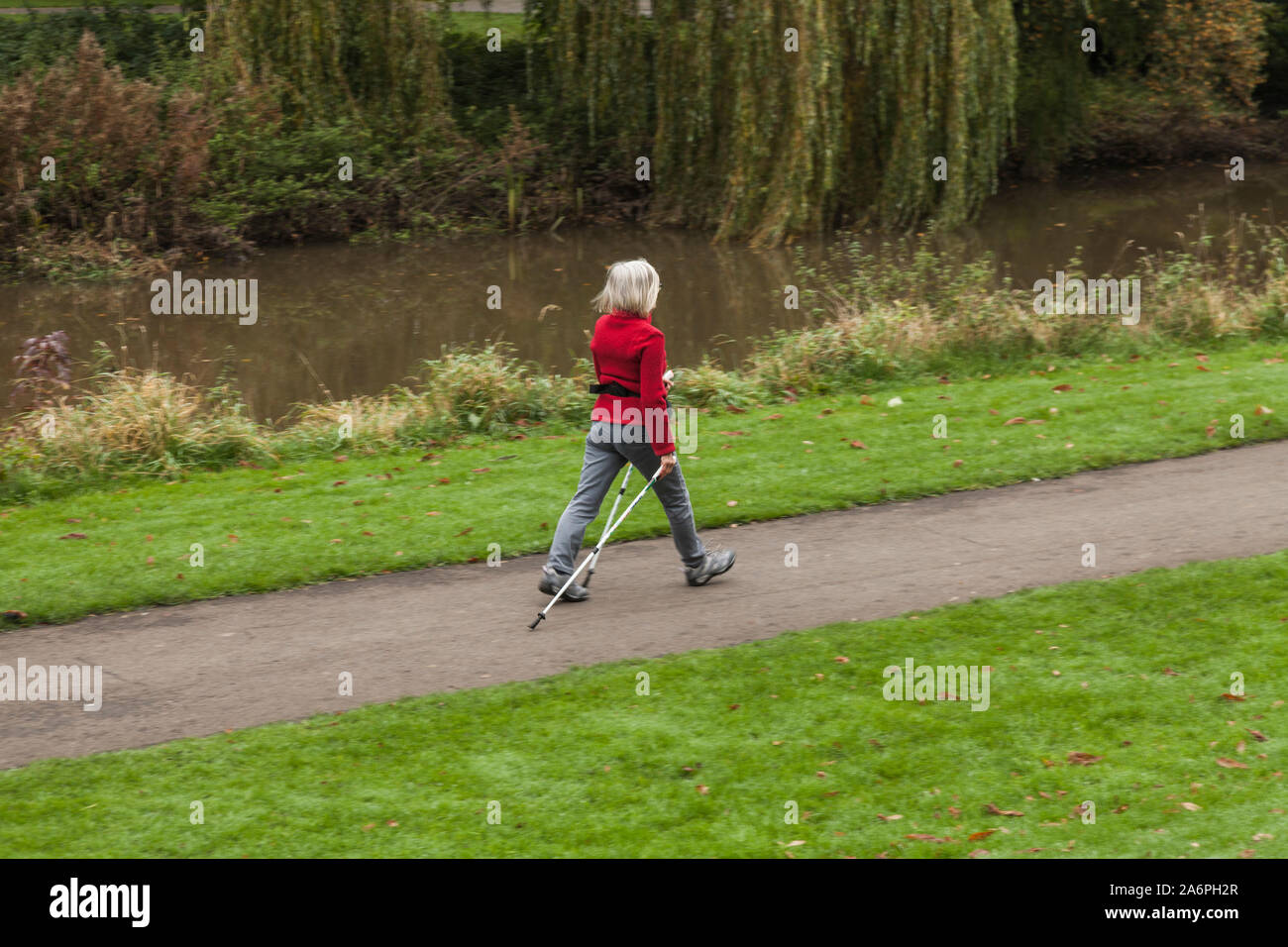 Eine Frau mit einer roten Jacke Nordic Walking im South Park, Darlington, England, Großbritannien Stockfoto