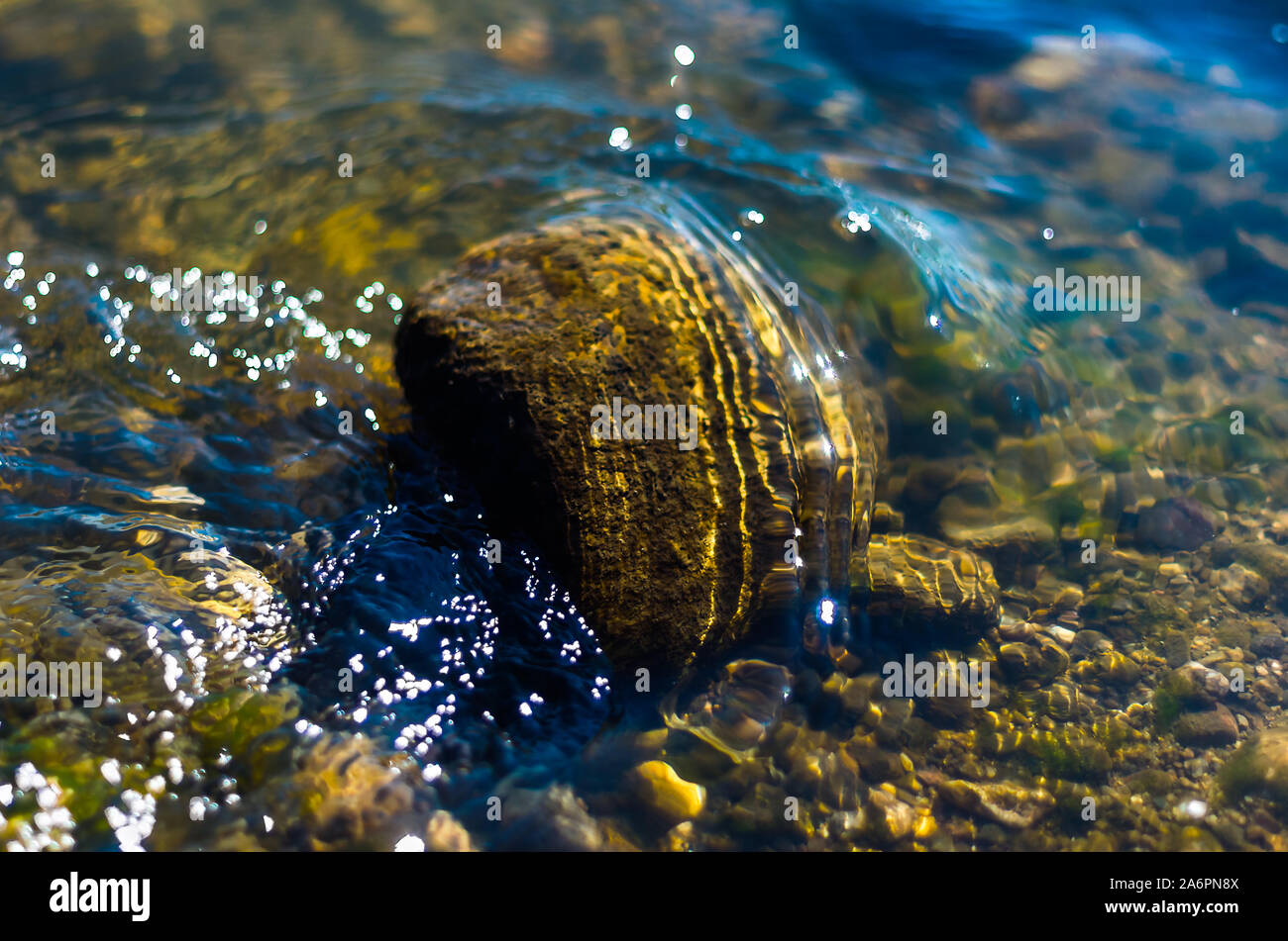 Spritzer von Fluss, der über einen großen Felsblock, Kiesel, Helle, sonnige Funkelt auf der Oberfläche. Stockfoto