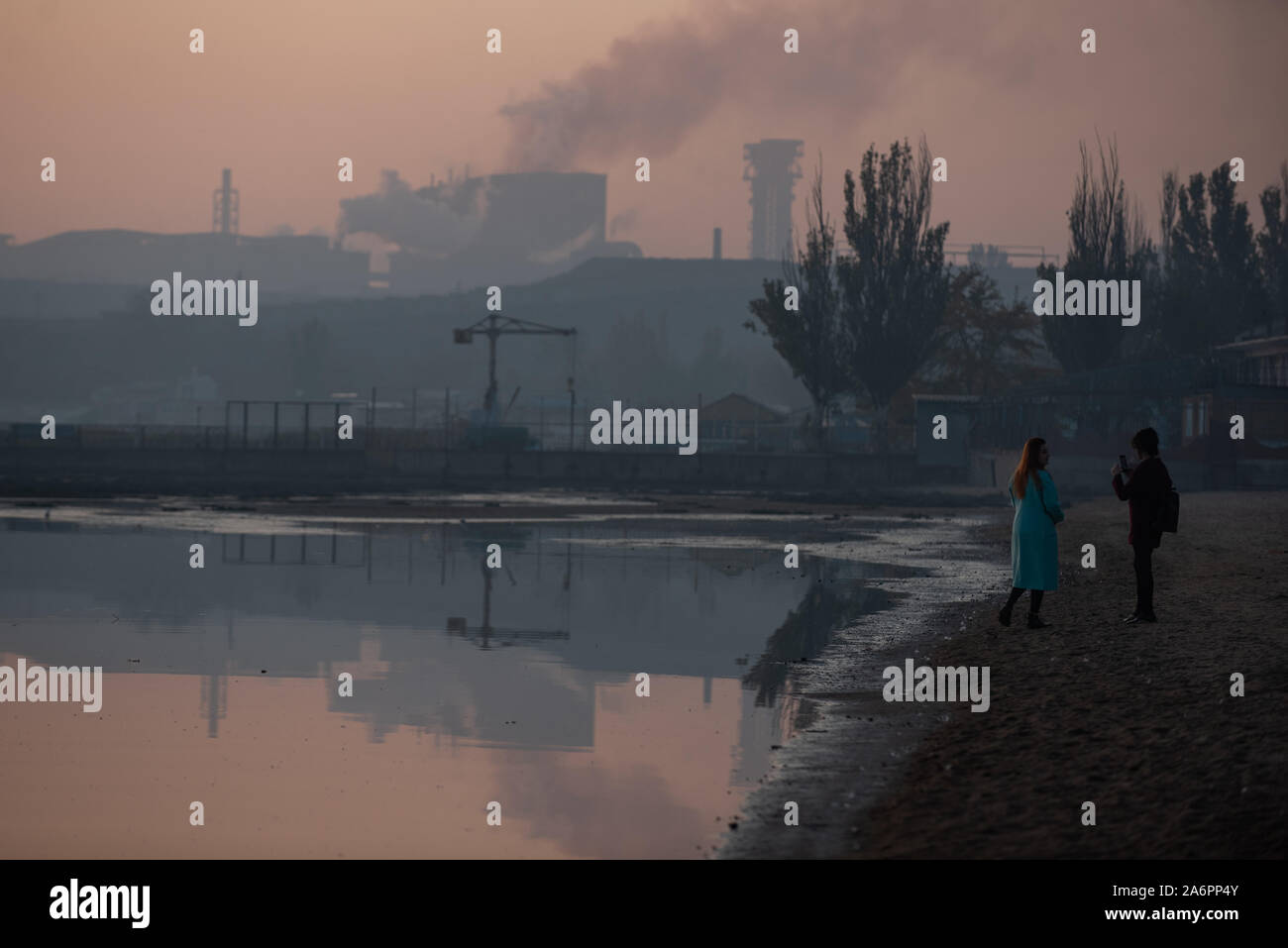 Frauen nehmen Fotos am Ufer des Asowschen Meeres in Mariupol. Die zwei großen metallurgischen Anlagen in Mariupol basieren die Azovstal Eisen- und Stahlwerke und die iljitsch Eisen- und Stahlwerke Teil Метинвест Gruppe. Nach Angaben der ukrainischen Ökologie Bericht des Ministeriums im Jahr 2016 Iljitsch Anlage mehr als 1,7 Millionen Tonnen gefährlicher Emissionen in die Atmosphäre erzeugt und Asowschen Stal produziert 78.600 Tonnen atmosphärischer Schadstoffe und schüttete 1,4 Millionen Kubikmeter Abfall in das Asowsche Meer. Im Jahr 2018 des Ukrainischen Gesundheitsministeriums warnte die öffentlichkeit Schwimmen an einem der Strände um Mariupol zu vermeiden. Stockfoto