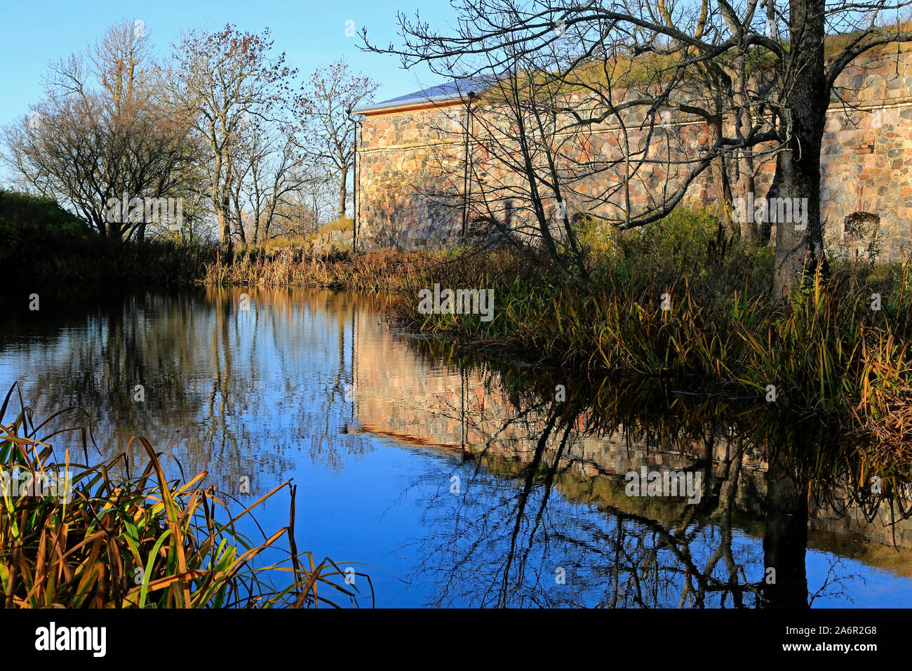 Kleiner Teich mit Reflexionen auf den blauen Himmel und Befestigungsanlagen in Piper's Park, Suomenlinna, die zum UNESCO-Weltkulturerbe in Helsinki, Finnland. Okt 2019 Stockfoto