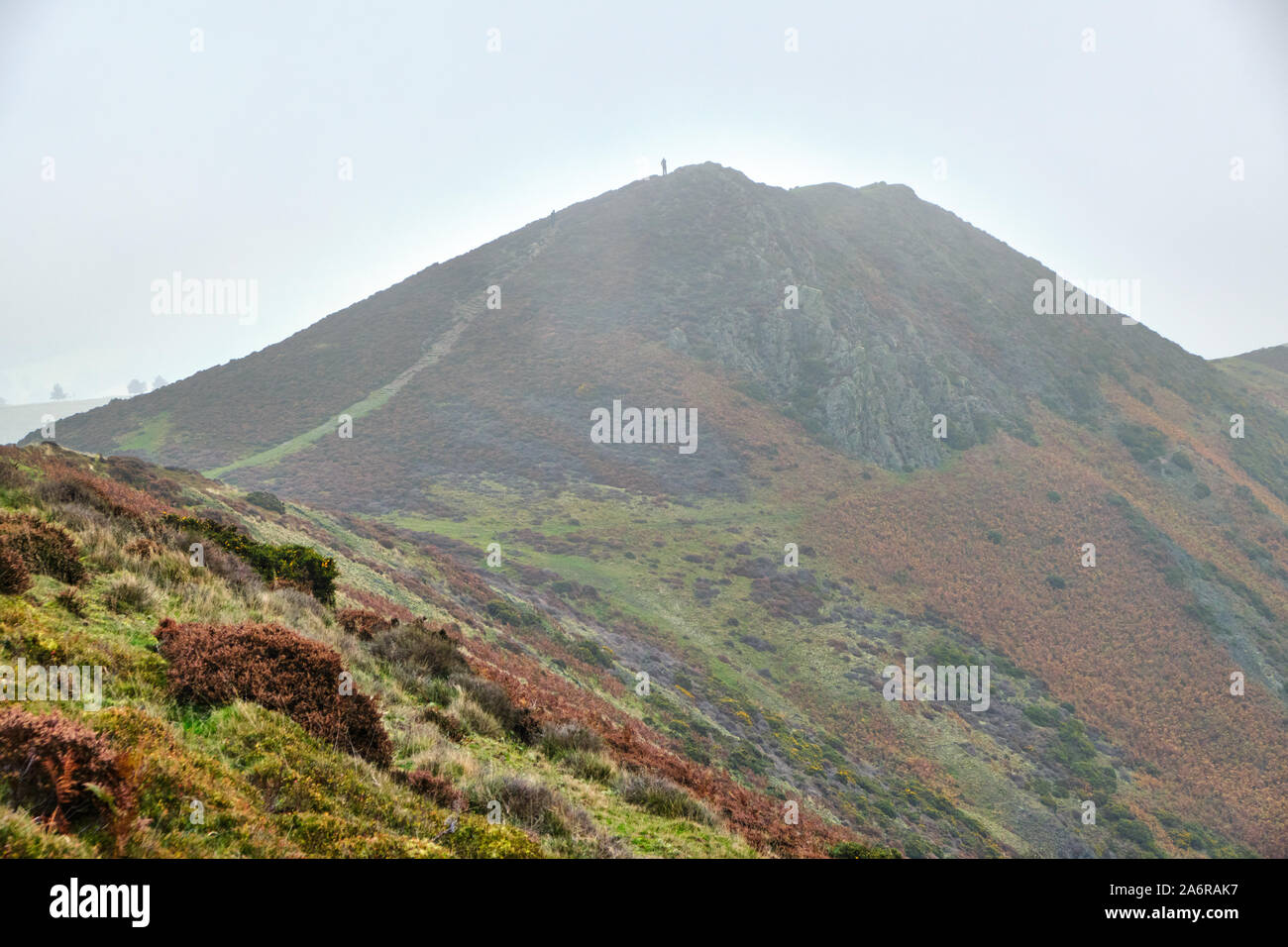 Burway Hill in der Nähe von Church Stretton in Shropshire im Herbst Nebel und niedrige Cloud mit einer Abbildung in der Ferne auf dem Gipfel Stockfoto