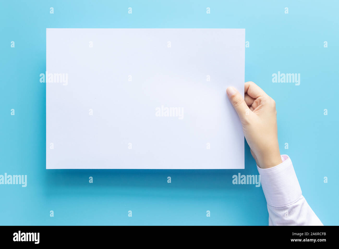 Die Hände schließen Holding leere weiße Leere schreiben Papierformat A4 für Flyer oder Einladung mock up auf einem blauen Hintergrund. Stockfoto