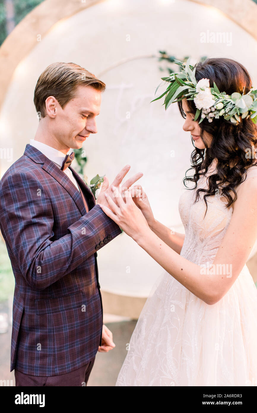 Hochzeit paar exchange Ringe auf Hochzeit im Freien. Braut mit einem Strauß Blumen und Grün und Bräutigam im eleganten Anzug mit Bogen auf Stockfoto