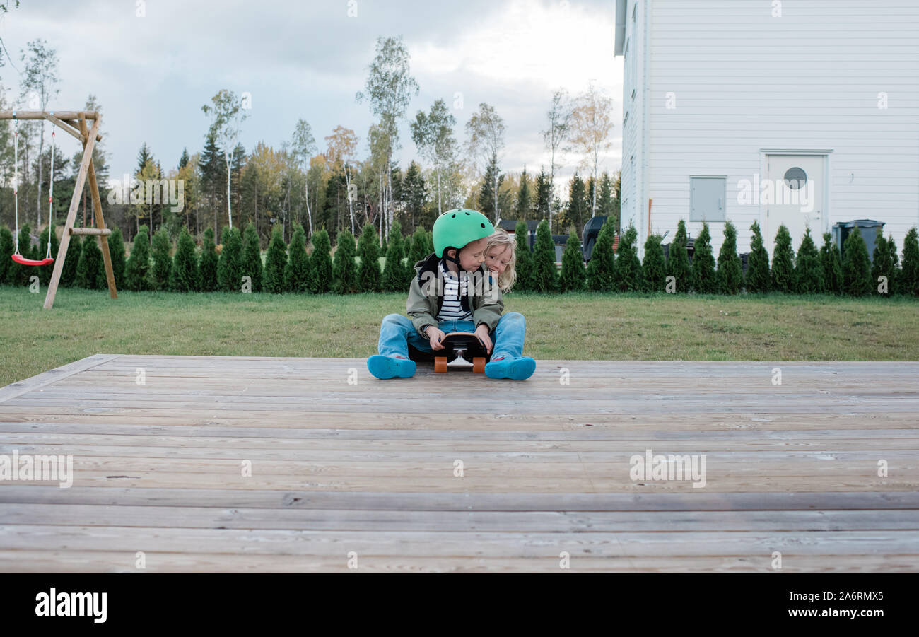 Bruder und Schwester spielen auf einem Skateboard in einem Garten Spaß Stockfoto