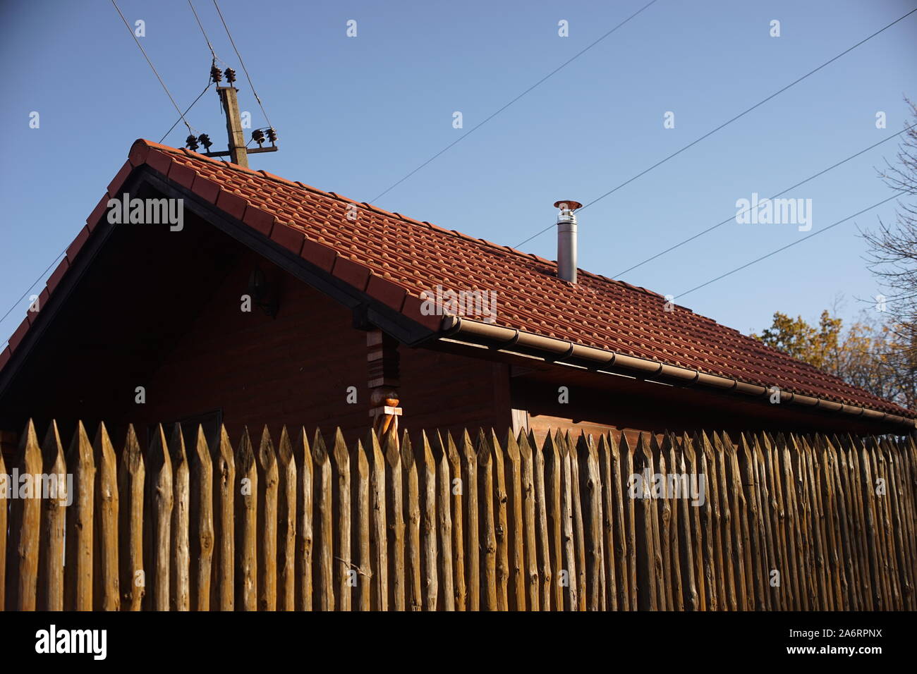 Holzhaus mit rotem Ziegeldach und blauer Himmel. Zaun aus spitzen Holzpfählen Stockfoto