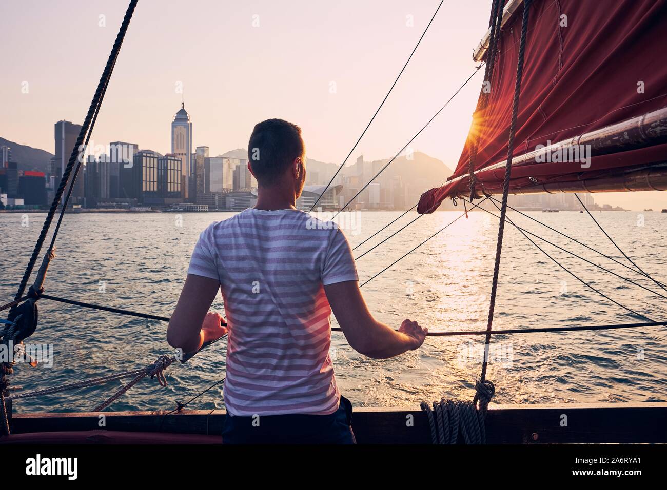 Reisenden, die auf traditionellen junk Boat Crossing Victoria Hafen gegen Hong Kong Stadtbild mit seinen Wolkenkratzern im Golden Sunset. Stockfoto