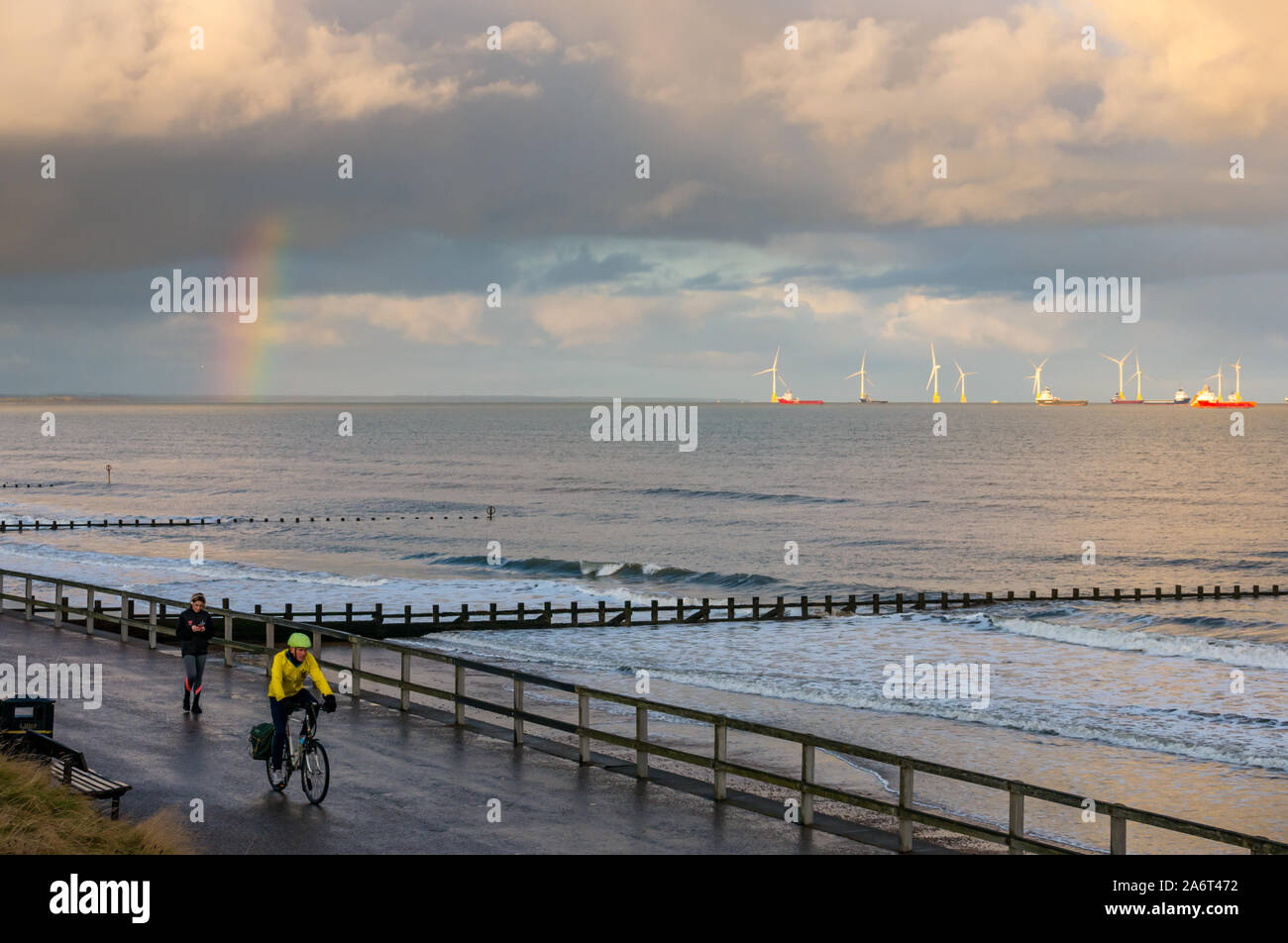 Strand von Aberdeen, Aberdeen, Schottland, Vereinigtes Königreich, 28. Oktober 2019. UK Wetter: Sonnenschein und Duschen in der Stadt eine helle Regenbogen bei Sonnenuntergang über der Nordsee in Richtung der Windpark in Aberdeen Bucht mit einem Radfahrer auf der Esplanade auf der Suche führen Stockfoto