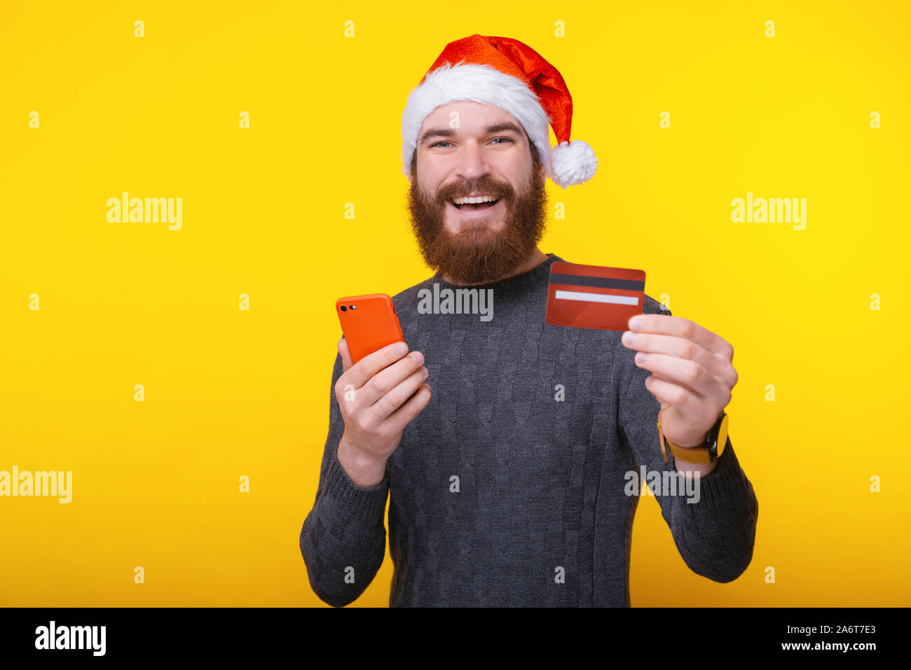 Freundliche Mann mit Bart und Santa Claus hat seine Kreditkarte und Holding Handy Stockfoto