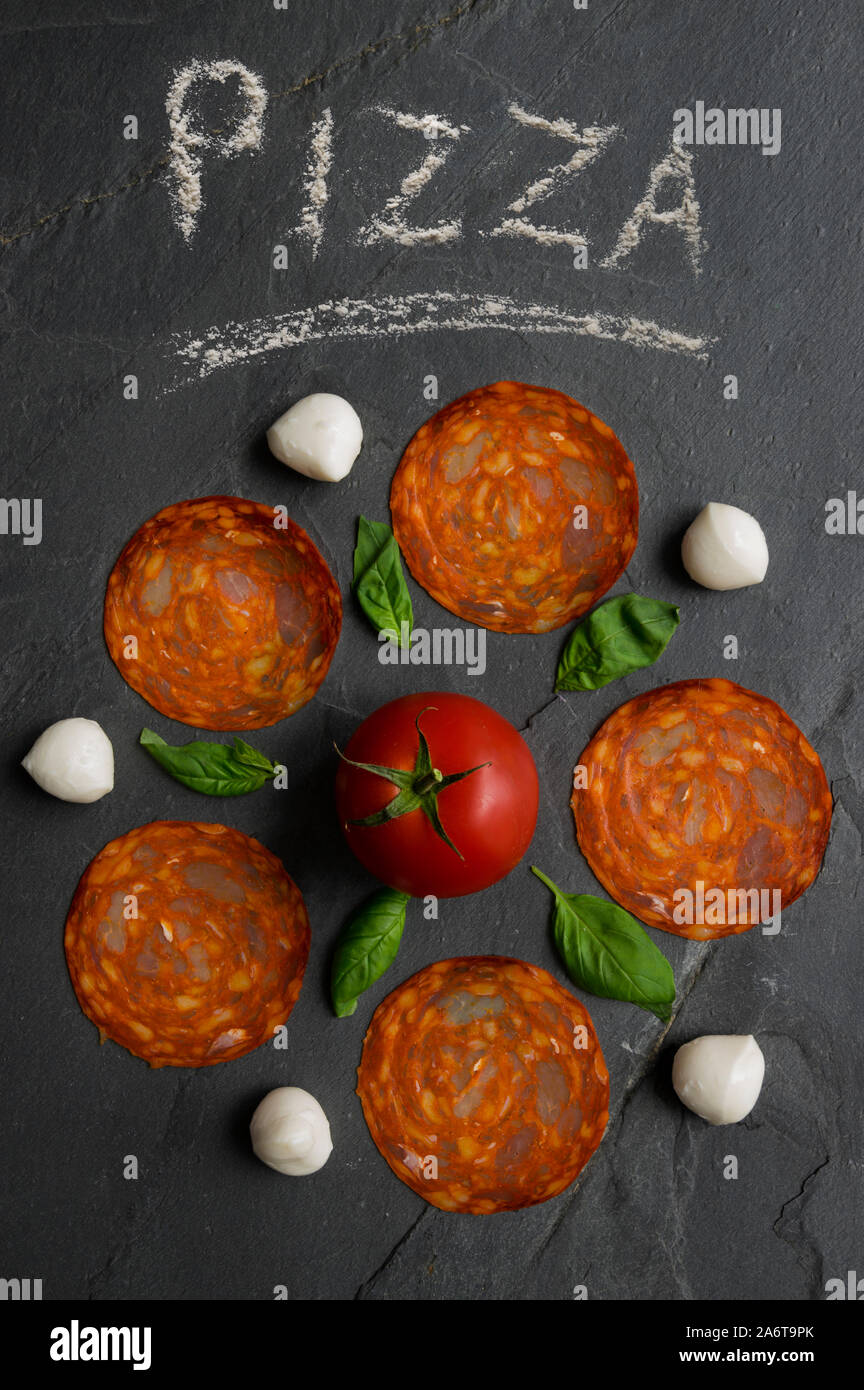 Traditionelle italienische Pizza Zutaten Mozzarella, Salami, Tomate und Basilikum besteht in einer Blume auf schwarzem Naturstein Hintergrund. Pizza Stockfoto