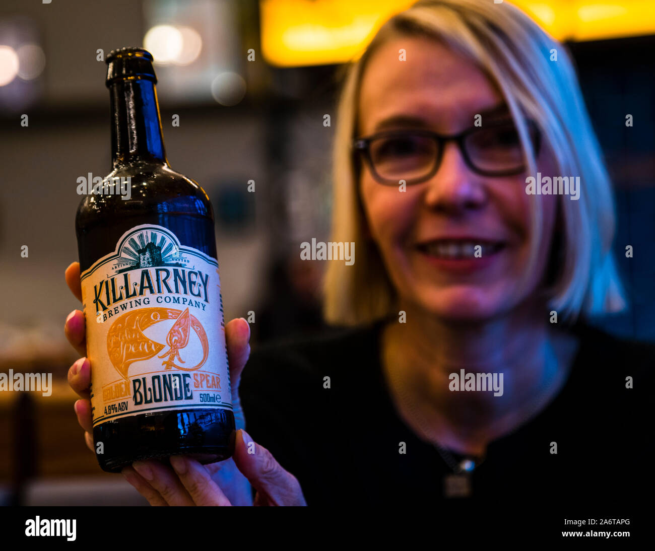 Blonde Girl präsentiert eine Flasche blondes Killarney Bier, Irland. Die Lebensmitteljournalistin Angela Berg ist ein großer Bierfan. In Irland stieß sie auf eine coole Blondine, die zu ihrer Haarfarbe passt Stockfoto