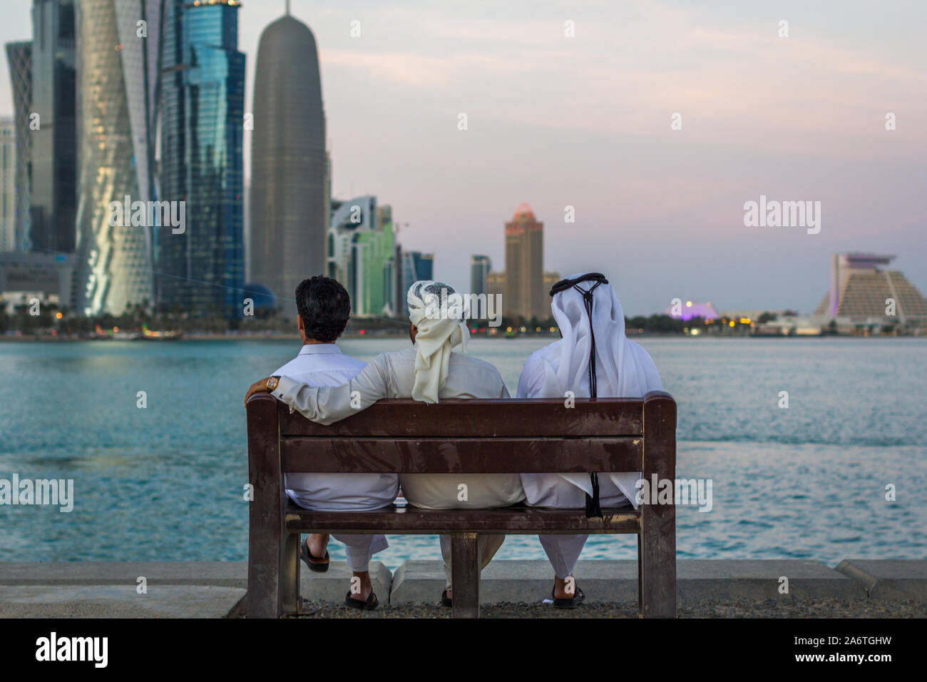 Drei arabische Menschen in traditioneller Kleidung sitzen auf einer Bank und blicken in den arabischen Golf in Doha Katar Stockfoto