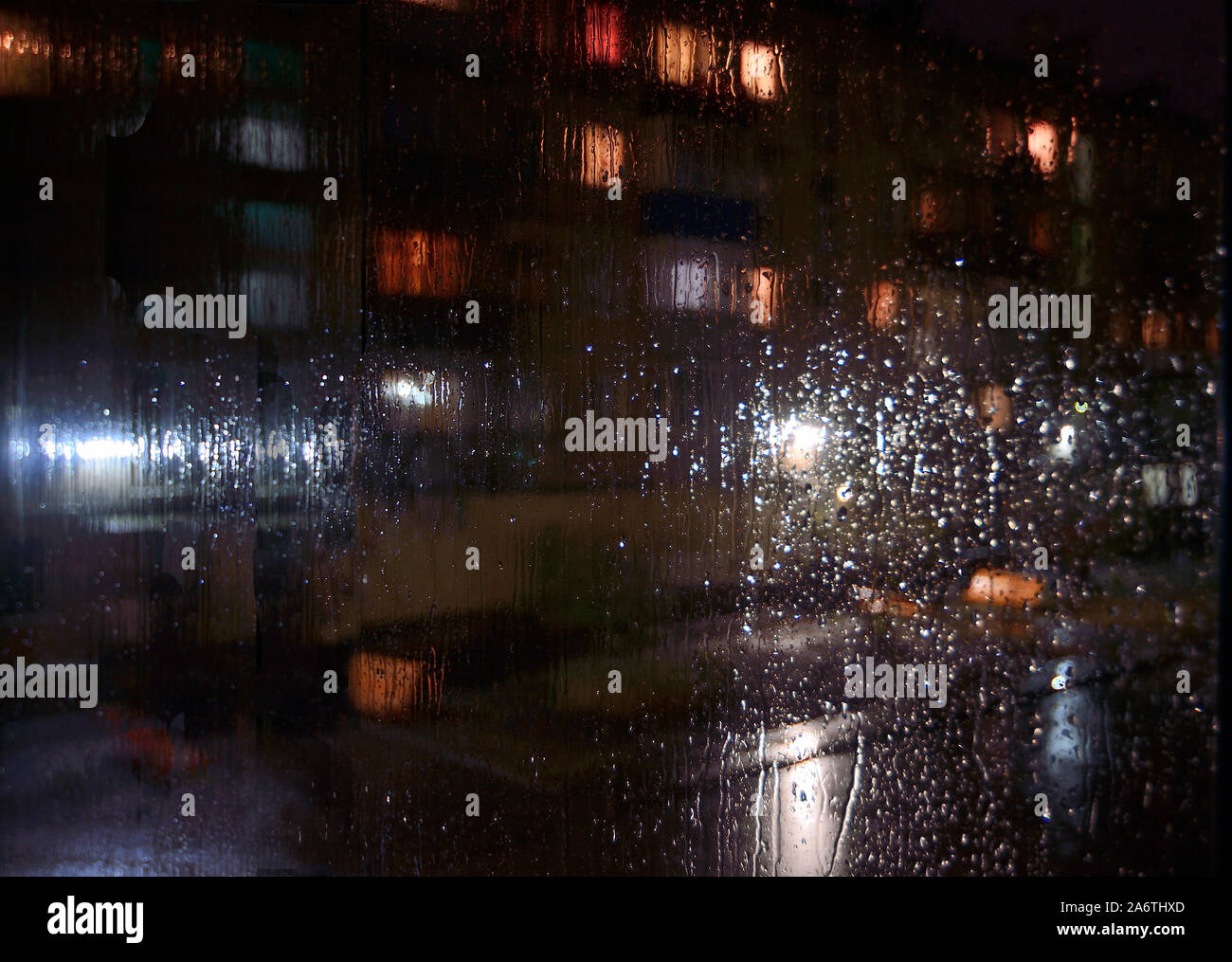 Nacht regnerischen sityscape außerhalb der Scheibe - Defokussierten verschwommenen Hintergrund mit Wassertropfen auf Glas, Bokeh der Nacht beleuchtung, geparkte Autos. Mela Stockfoto