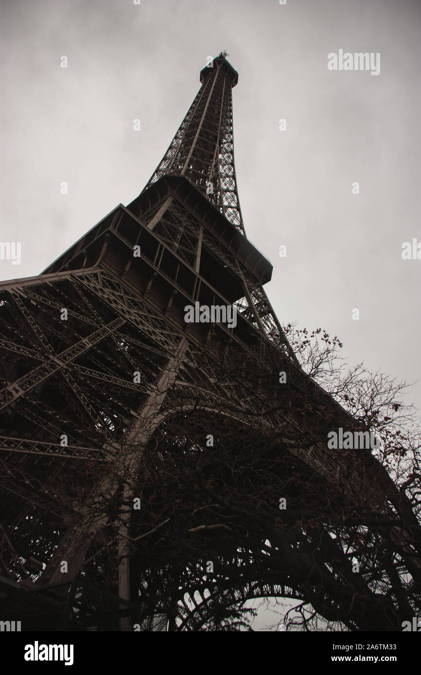 Extreme Low Angle Eiffelturm und Bäume in seinen Fuß in einem bewölkten Tag in Paris, Frankreich - Vertikaler das Wahrzeichen der Stadt der Liebe - Eu Stockfoto