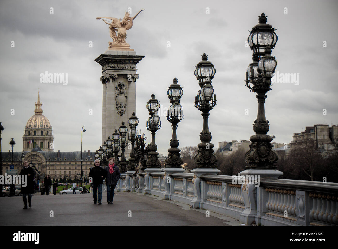 Ein Paar zu Fuß über die Brücke Alexander III in Paris - alten schmiedeeisernen Lampen auf der rechten Seite - bewölkten Tag in der Pariser City National P Stockfoto
