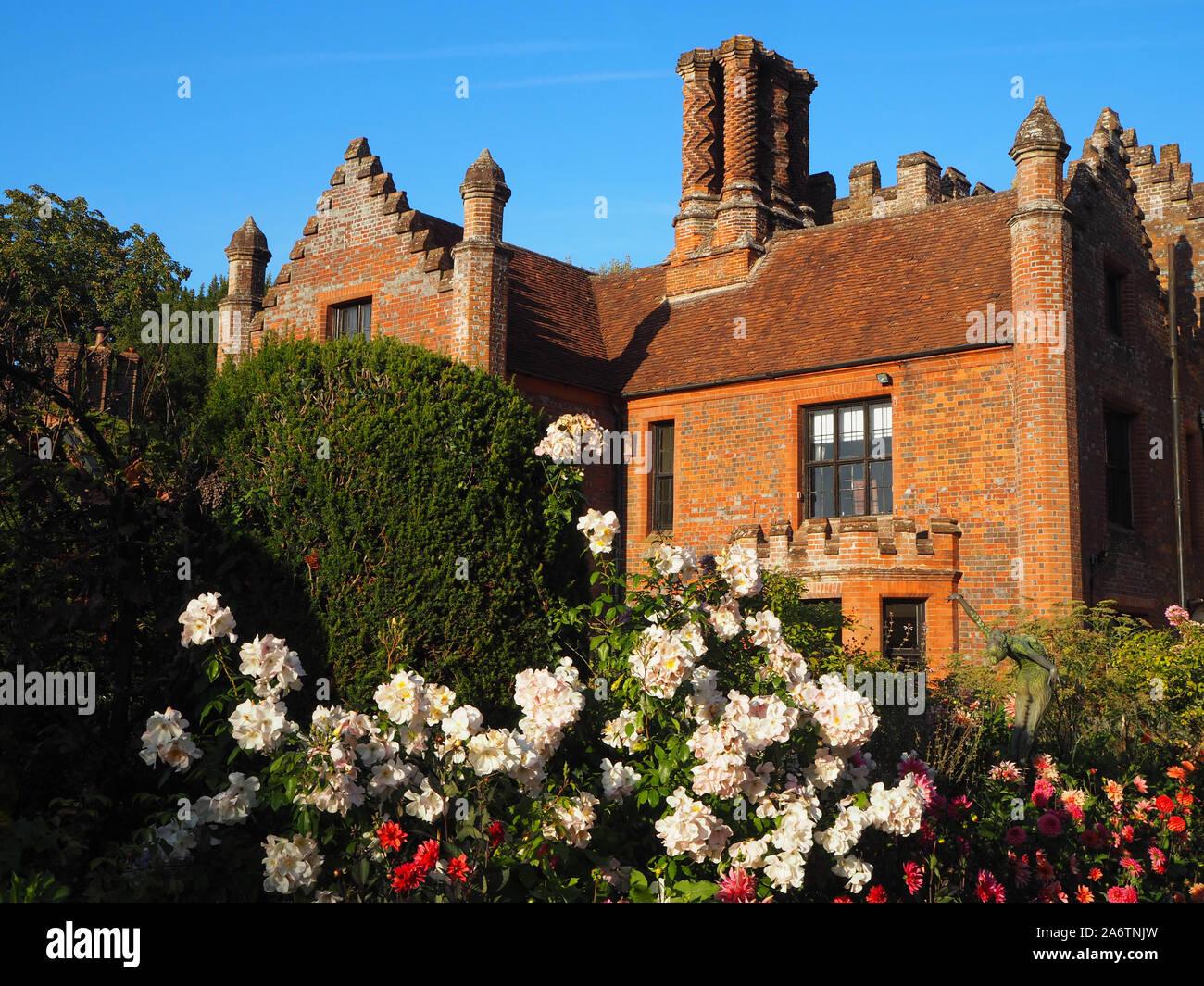 Chenies Manor Haus und Garten im Spätsommer an einem schönen Abend. Pastellfarbenes creme Rosen, vibrant pink Dahlien, blauer Himmel und hohen Bäumen Rahmen der Szene. Stockfoto