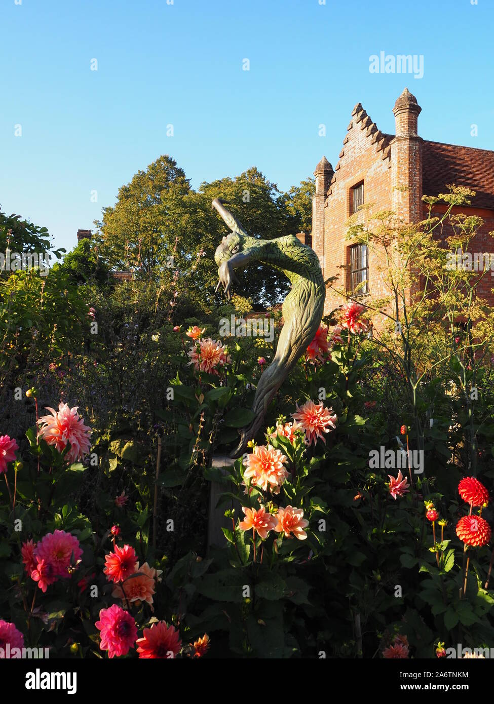 Chenies Manor Haus und Garten im Spätsommer an einem schönen Abend. hell rosa Dahlie Sorten, blauer Himmel, hohe Bäume Rahmen. Eine Skulptur erreicht. Stockfoto