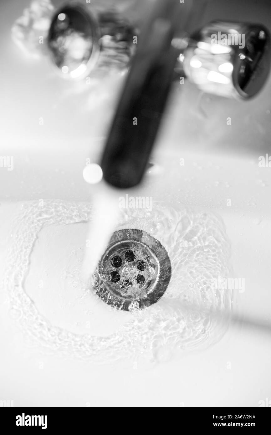 Ein Bach mit sauberem Wasser fließt in die Ablassöffnung des weißen Waschbecken mit einer geringen Tiefenschärfe Stockfoto