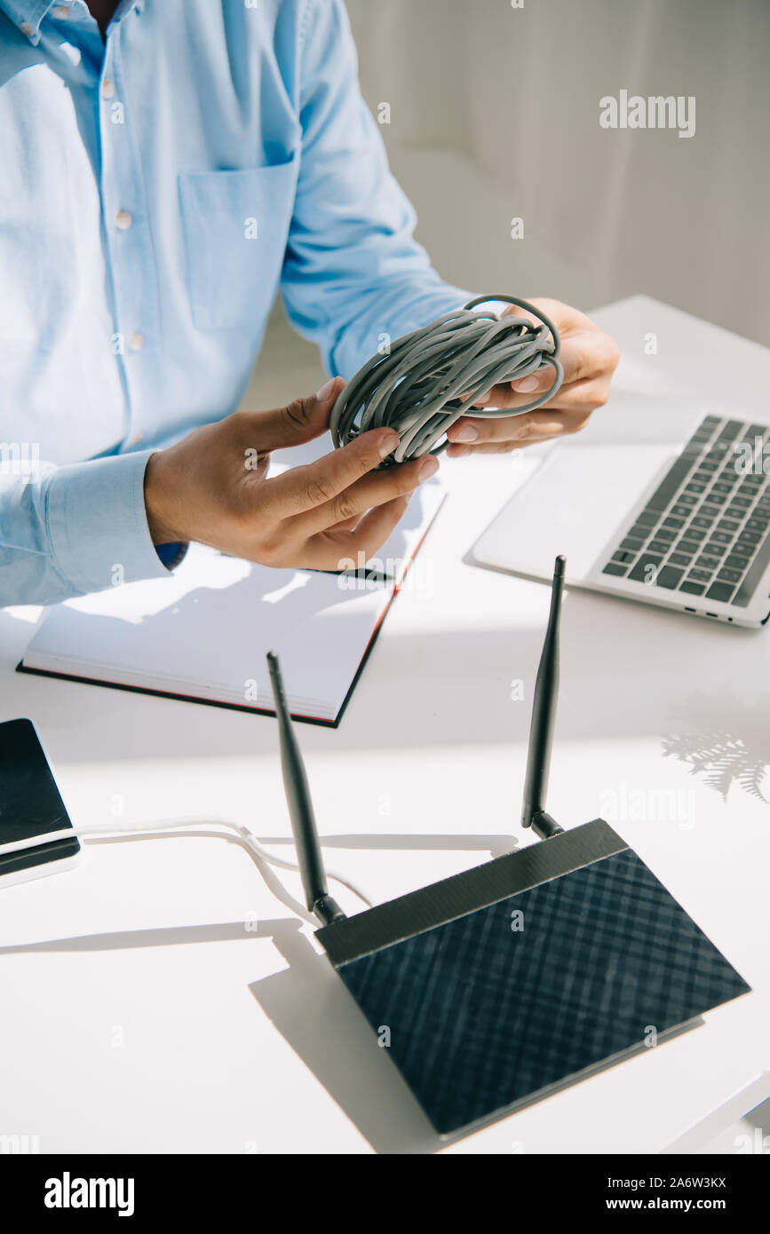 7/8-Ansicht des Geschäftsmannes holding Draht in der Nähe von Router gesteckt und Laptop Stockfoto