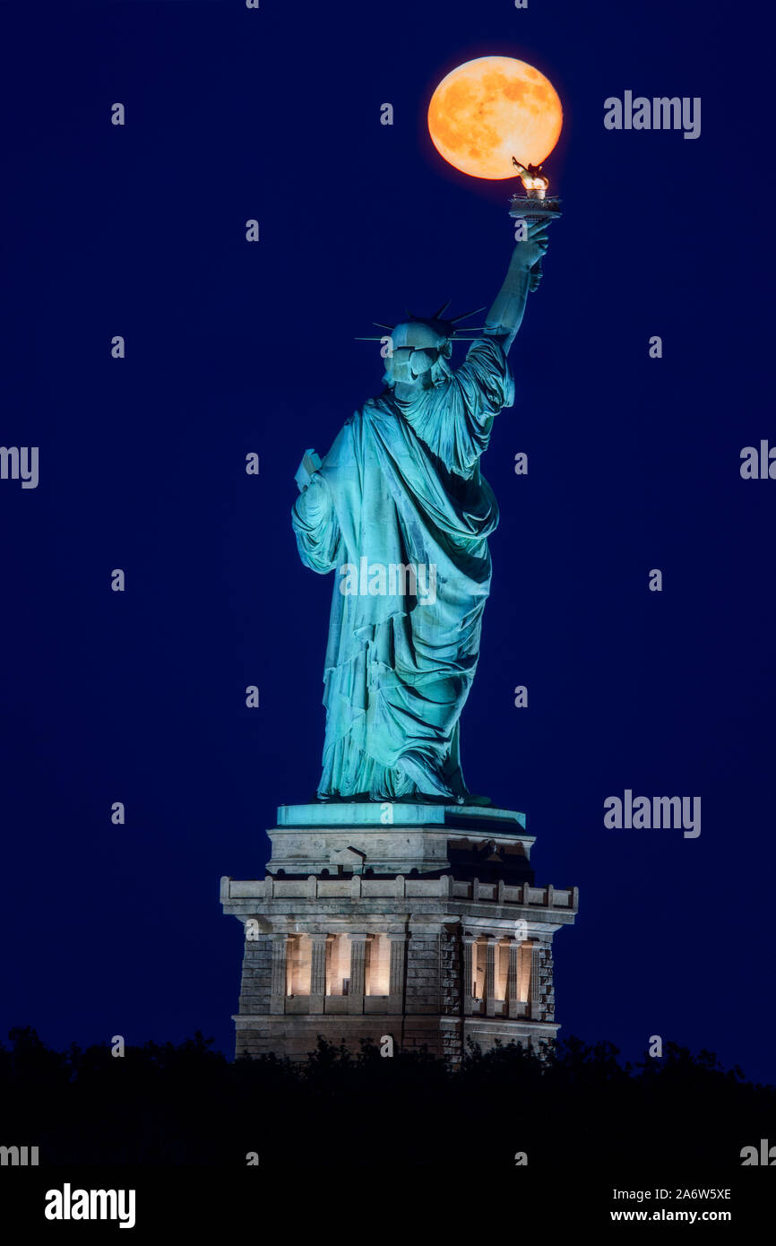 Die super Mond erhebt sich über der Freiheitsstatue während der Blauen Stunde der Vollmond-Leitungen, die perfekt mit den Statuen Fackel. Stockfoto