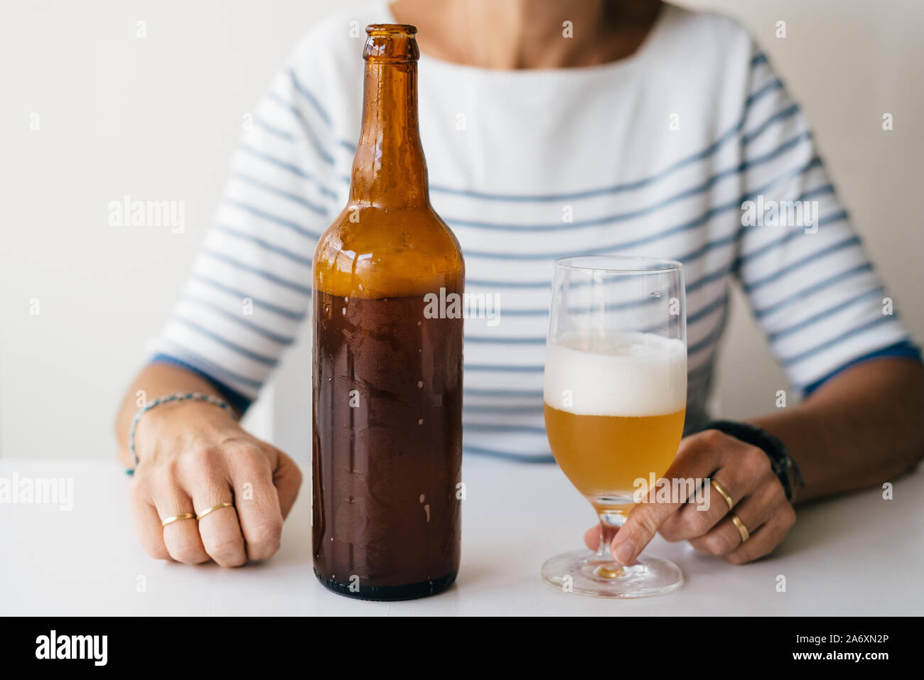 Frau sitzt an einem Tisch mit einem Glas Bier und einer Flasche. Stockfoto